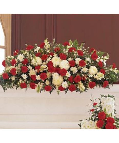 An arrangement of red and white flowers with green leaves sits on a ledge in a room with maroon walls and a window nearby.