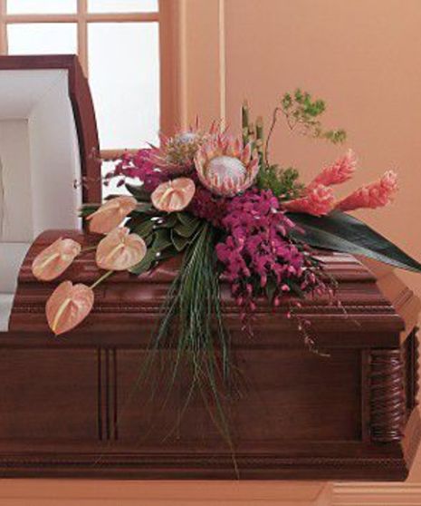 Wooden coffin adorned with a floral arrangement consisting of pink and white flowers and green leaves; placed in a room with peach-colored walls 