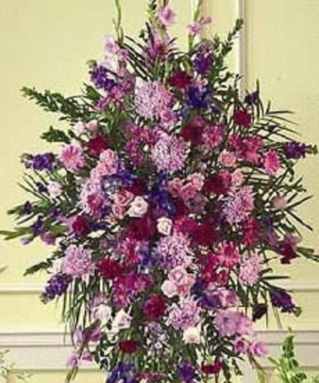 An arrangement of pink, purple, and white flowers with green foliage displayed vertically on a pale yellow wall, accentuated by elegant paneling in the background.