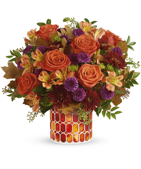 A bouquet of orange roses, purple chrysanthemums, and autumn leaves arranged in a vase with red and orange hexagonal patterns set against a white background.