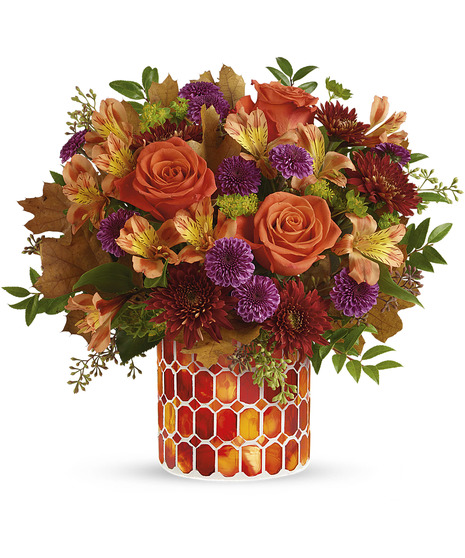 A bouquet of orange roses, purple chrysanthemums, and autumn leaves arranged in a vase with red and orange hexagonal patterns set against a white background.
