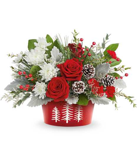 A festive arrangement of red roses, pinecones, and lush greenery sits in a red vase adorned with a cardinal bird design, complemented by white flowers and red berry accents.