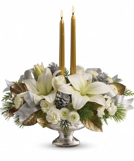 A silver vase holds a holiday bouquet of white lilies, pinecones, and greenery, accentuated by two lit gold candles and decorative silver and gold leaves.