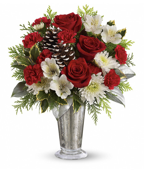 A bouquet of red roses, white lilies, and pinecones arranged in a silver vase, surrounded by greenery against a white background.