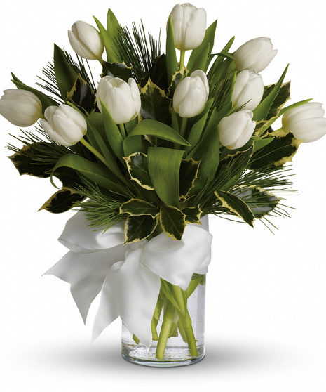 A bouquet of white tulips arranged in a cylindrical glass vase with water, accented by green foliage and adorned with a large white ribbon in a bow.