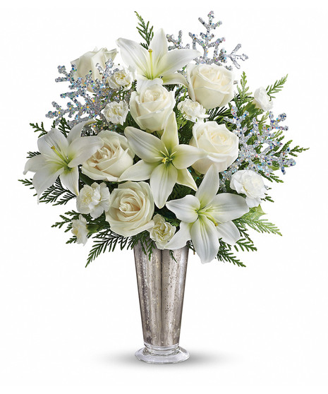A silver vase holds white roses, carnations, and greenery, adorned with glittery, silver snowflake decorations, set against a plain white background.