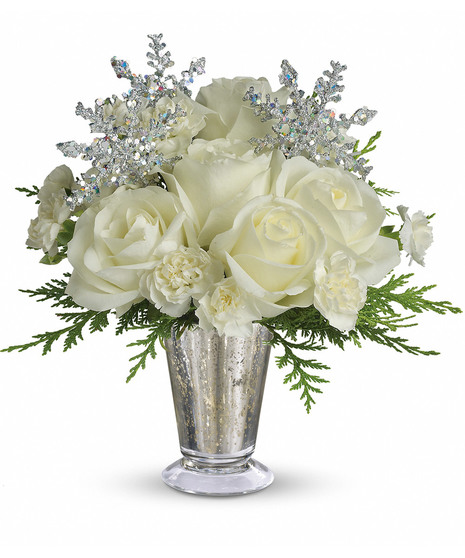 A silver vase holds white roses, carnations, and greenery, adorned with glittery, silver snowflake decorations, set against a plain white background.