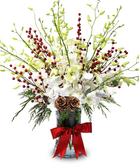 A floral arrangement featuring white flowers and red berries is displayed in a clear vase adorned with a red ribbon bow. 
